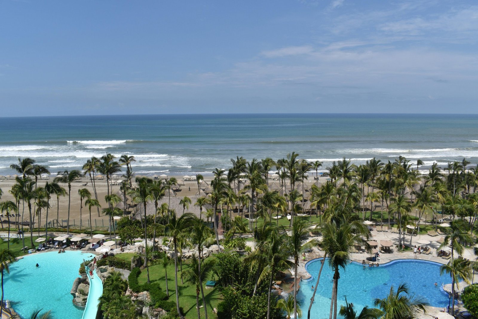 A panoramic view of palm trees, pools, and ocean in Acapulco.
